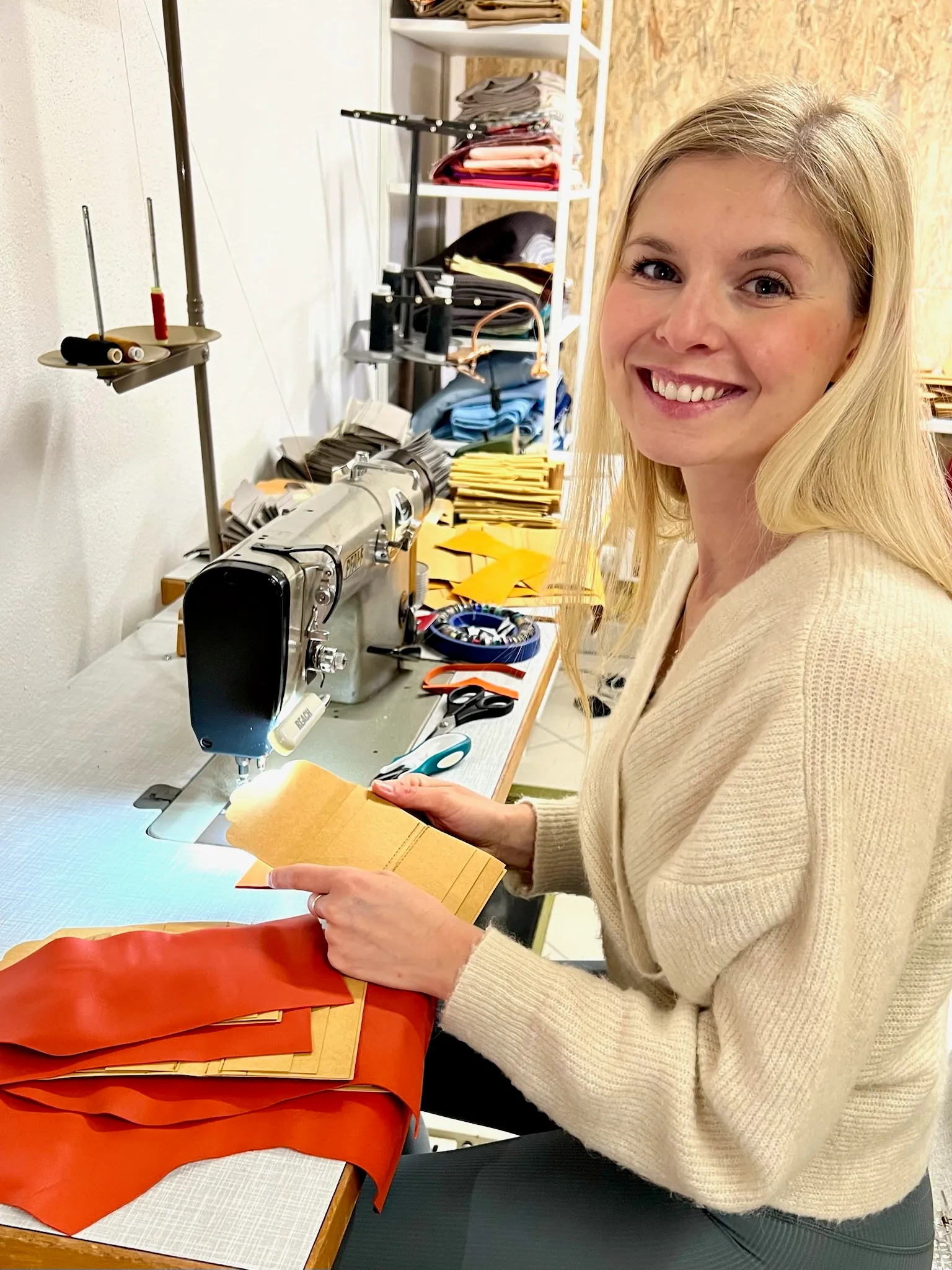 Die Macherin an der Nähmaschine, lächelnd mit orangefarbenem Leder in der Hand